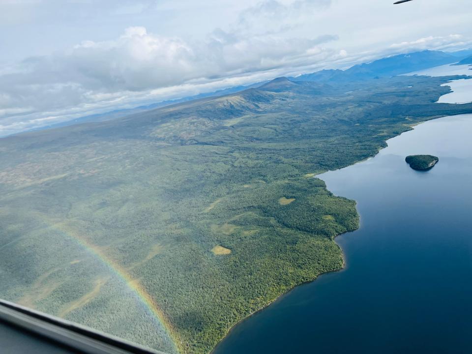 A rainbow over lush greenery is seen from the window of the plane.