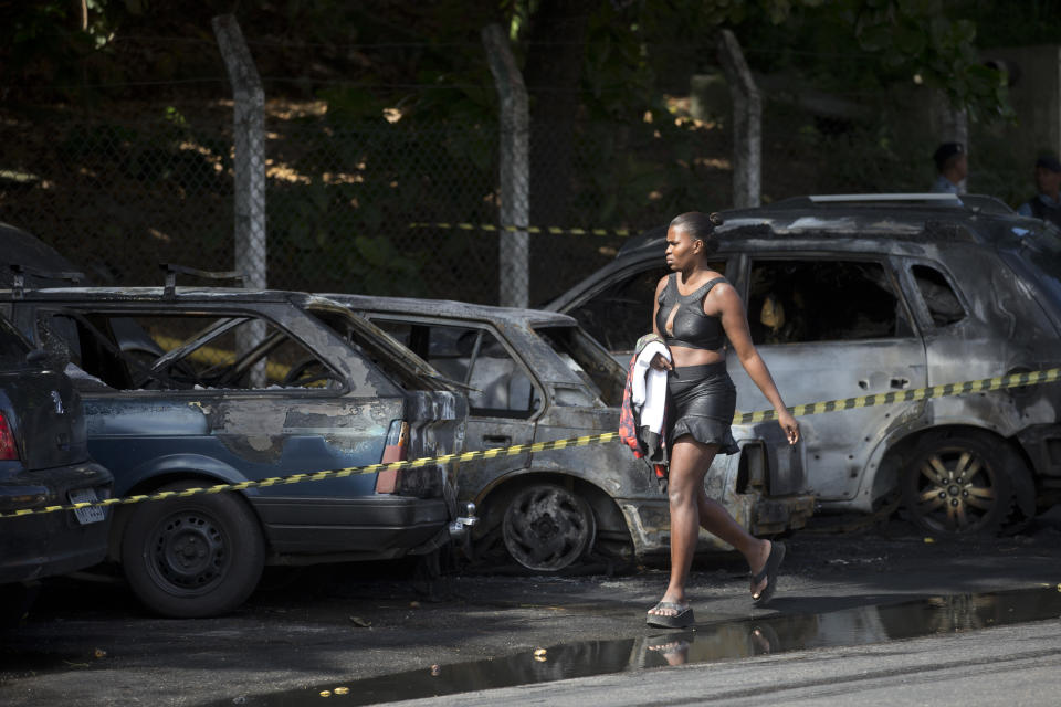 A woman walks past three cars that were set on fire by protestors demonstrating against the death of an elderly woman who died yesterday during a police operation against suspected drug traffickers in the Complexo do Alemao of Rio de Janeiro, Brazil, Monday, April 28, 2014. The woman who died is Arlinda Bezerra das Chagas, age 72. (AP Photo/Silvia Izquierdo)