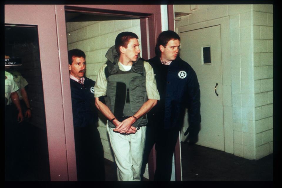 timothy mcveigh, wearing tan prison clothes and a bulletproof vest, is escorted by two officers out of a courthouse room