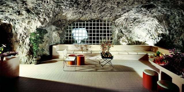 cave room with spare furniture with a very long white banquette and some red stools as highlight
