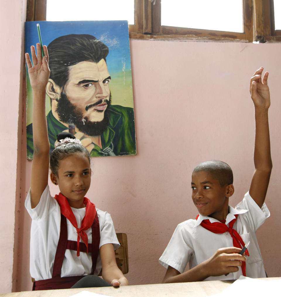 This April 24, 2012 photo shows students raising their hands to answer their teacher's questions in front of a portrait of Ernesto "Che" Guevara, the Argentine-born co-founder of the Cuban revolution, at the Jose Maria Heredia Vocational Arts school in Santiago de Cuba, Cuba. The school is dedicated to educating musically- talented eight to 18 year-olds, some of whom come from surrounding areas. The Cuban government provides free tuition, room and board. Students are allowed to return home every two weeks to visit their families.(AP Photo/Kathy Willens)