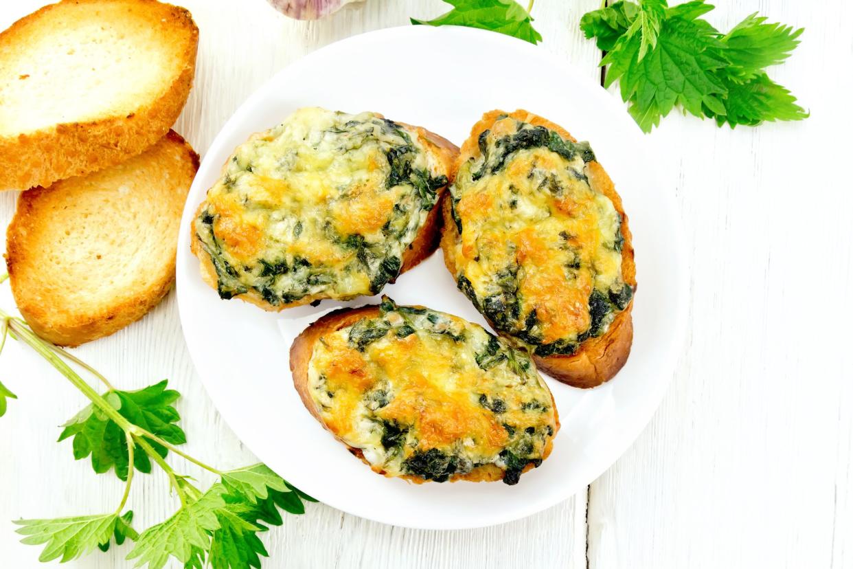 Hot sandwiches with nettles and cheese on slices of wheat bread in a plate on a wooden board background from above