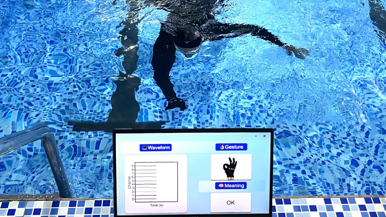  A diver in a swimming pool makes a hand gesture, which is translated into words on a screen. 