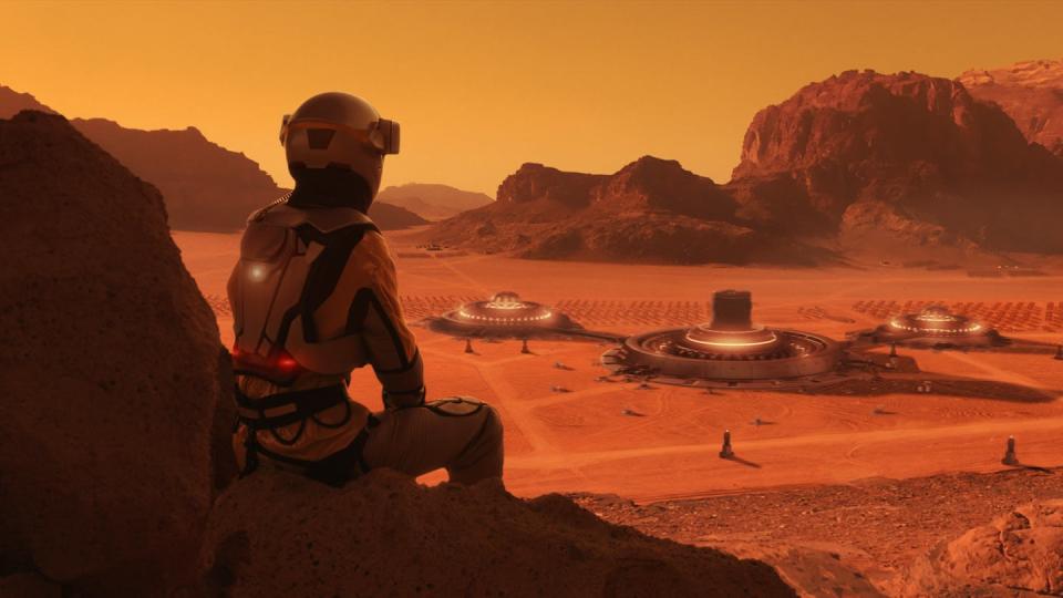 An artistic concept of an astronaut on Mars, sitting against a rock and looking at the space colony situated in the distance on a dusty, orange plain.