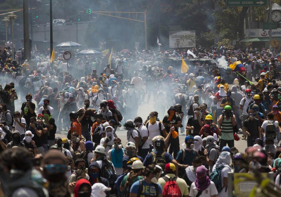 Anti-government demonstrators run from a cloud of tear gas fired at them by Bolivarian National Police during clashes at the Central University of Venezuela, UCV, in Caracas, Venezuela, Thursday, March 20, 2014. Thursday dawned with two more opposition politicians, San Cristobal Mayor Daniel Ceballos and San Diego Mayor Enzo Scarano, behind bars. Police used tear gas and water cannons to disperse a student-called protest of several thousand people in Caracas, some of those demonstrating against the arrests of the mayors. (AP Photo/Esteban Felix