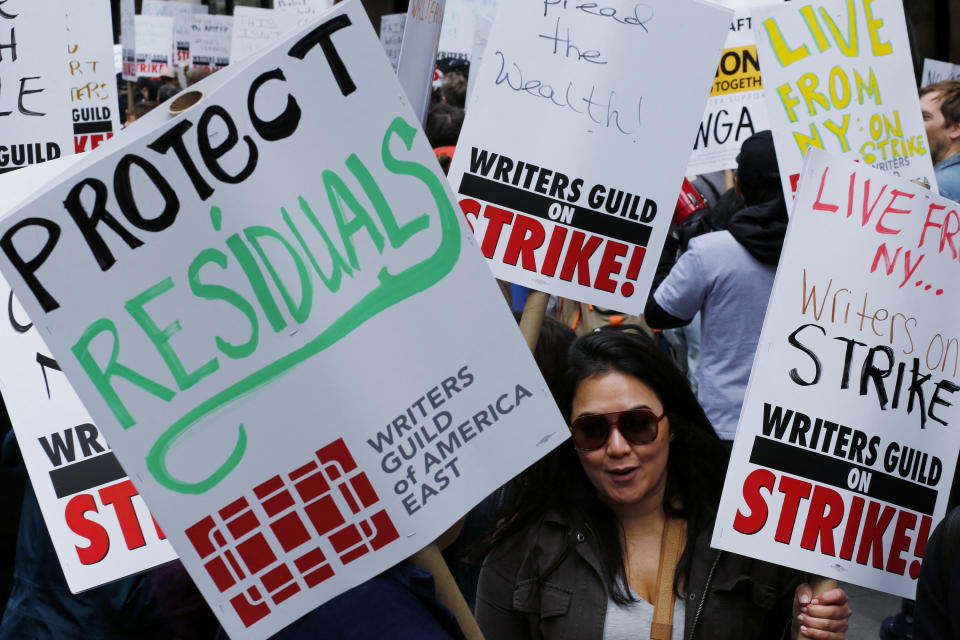 A WGA supporter with picket signs that say Protect Residuals and Live from NY...Writers Guild on Strike