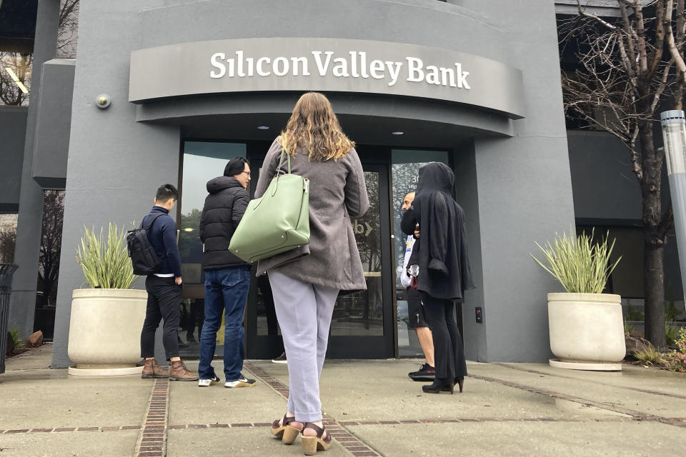 File - Des personnes se tiennent devant l'entrée de la Silicon Valley Bank à Santa Clara, en Californie, le vendredi 10 mars 2023. L'effondrement de la Silicon Valley Bank et de la Signature Bank, ainsi que le renflouement de la First Republic, ont été un choc pour les petites entreprises de toutes sortes, incitant nombre d'entre elles à examiner de près leurs services bancaires et à se demander s'il convient ou non d'apporter des changements pour garantir la sécurité de leur argent. (AP Photo/Jeff Chiu, File)