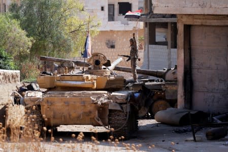 A Syrian army soldier holds a Syrian flag as he stands on a military vehicle in Khan Sheikhoun, Idlib