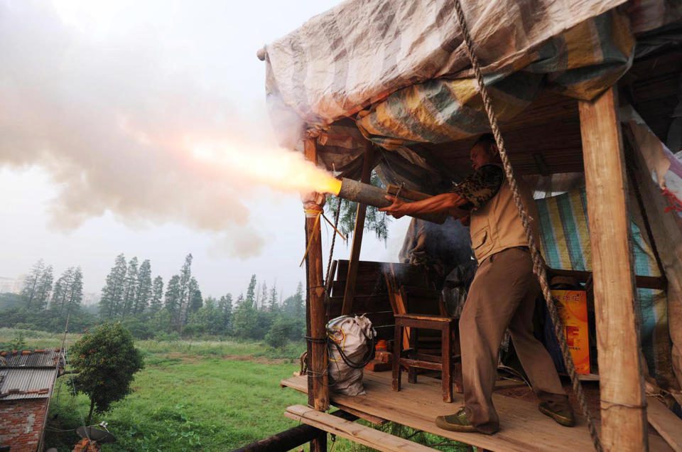 In a picture taken on June 6, 2010 Chinese farmer Yang Youde fires his homemade cannon near his farmland on the outskirts of Wuhan, in central China's Hubei province. Yang's improvised cannons, which are made out of a wheelbarrow, pipes and fire rockets, are used to defend his fields against property developers who want his land. Land seizures have been a problem for years in China, and have given rise to the term "nail house" to describe a holdout tenant or occupant, likening them to a nail refusing to be hammered down. CHINA OUT AFP PHOTO (Photo credit should read STR/AFP via Getty Images)