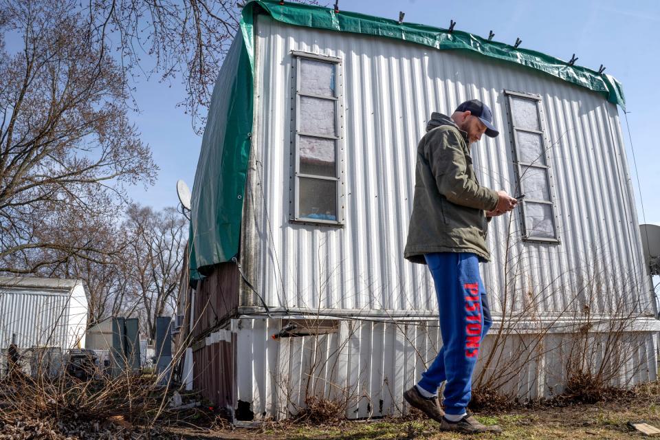 Landmark Estates resident Mark Brown looks at his phone next to his trailer at the mobile home park in Warren on Monday, Feb. 26, 2024, that he places a tarp on to keep the water from pouring in after a tree branch fell on it.