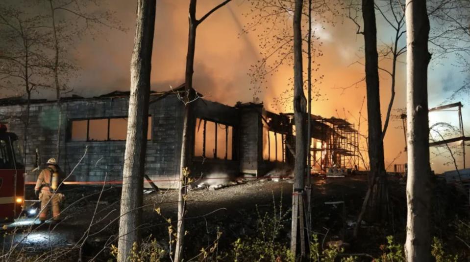 A firefighter is seen from the back and facing a large burning house.