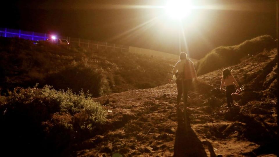 Una mujer camina en el lado estadounidense de la frontera con México junto a una niña.