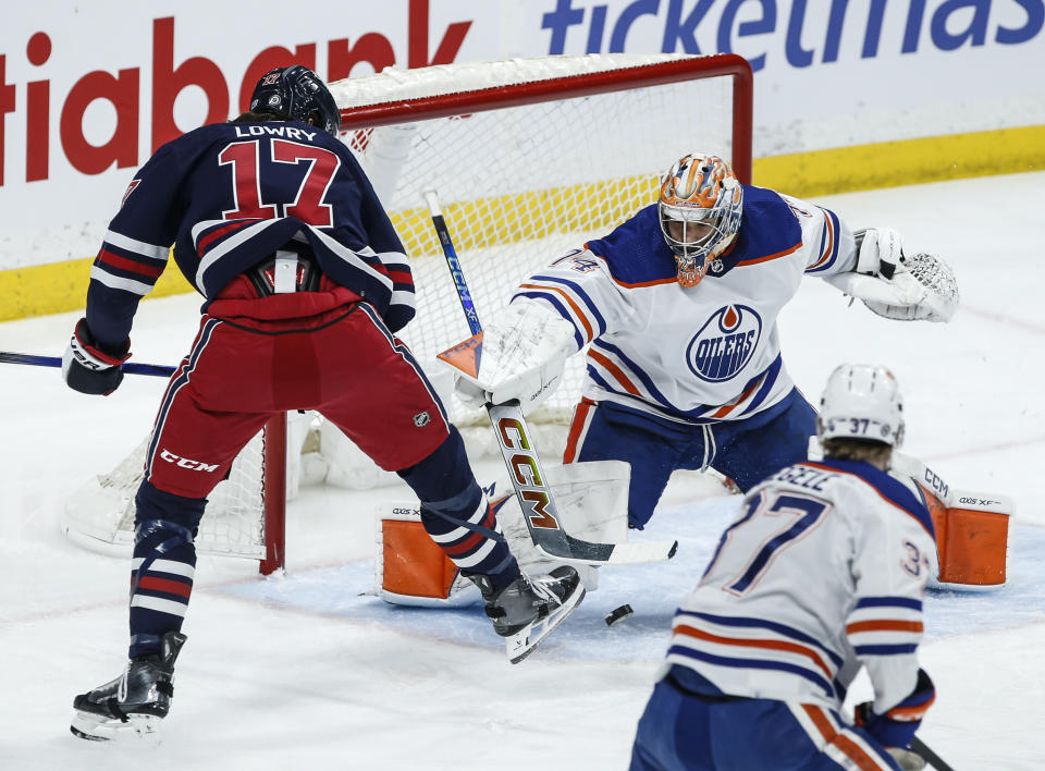 Winnipeg Jets' Adam Lowry (17) tries to gain control of the bouncing puck in front of Edmonton Oilers goaltender Stuart Skinner (74) during the first period of an NHL hockey game Tuesday, March 26, 2024, in Winnipeg, Manitoba. (John Woods/The Canadian Press via AP)