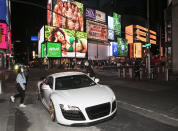 In this Saturday, May 2, 2020 photo, Claudia Luong, left, and Danny Lin hop into his 2008 Audi R8 for a spin around New York's Times Square during the coronavirus pandemic. Car mavens normally wouldn't dare rev their engines in Midtown, but now they're eagerly driving into the city to take photos and show off for sparse crowds walking through the commercial hub. (AP Photo/Mark Lennihan)