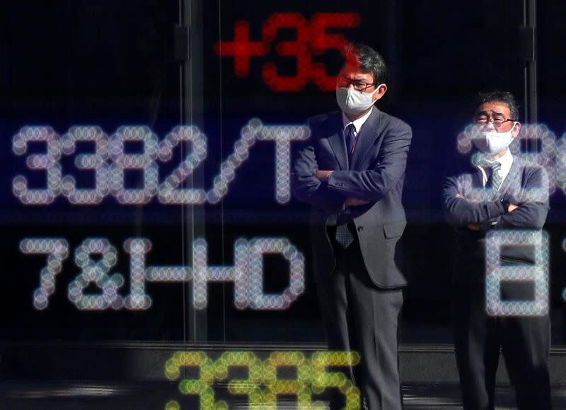 Passersby wearing protective face masks are reflected on a stock quotation board outside a brokerage, amid the coronavirus disease (COVID-19) outbreak, in Tokyo