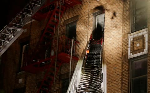 A ladder from a fire truck extends to an apartment window where firefighters respond to a deadly fire - Credit: Frank Franklin/AP