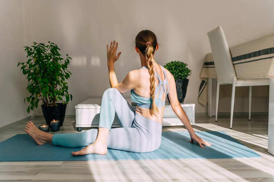 Mid adult woman doing yoga at home on a sunny day. Indoor plants in the background.