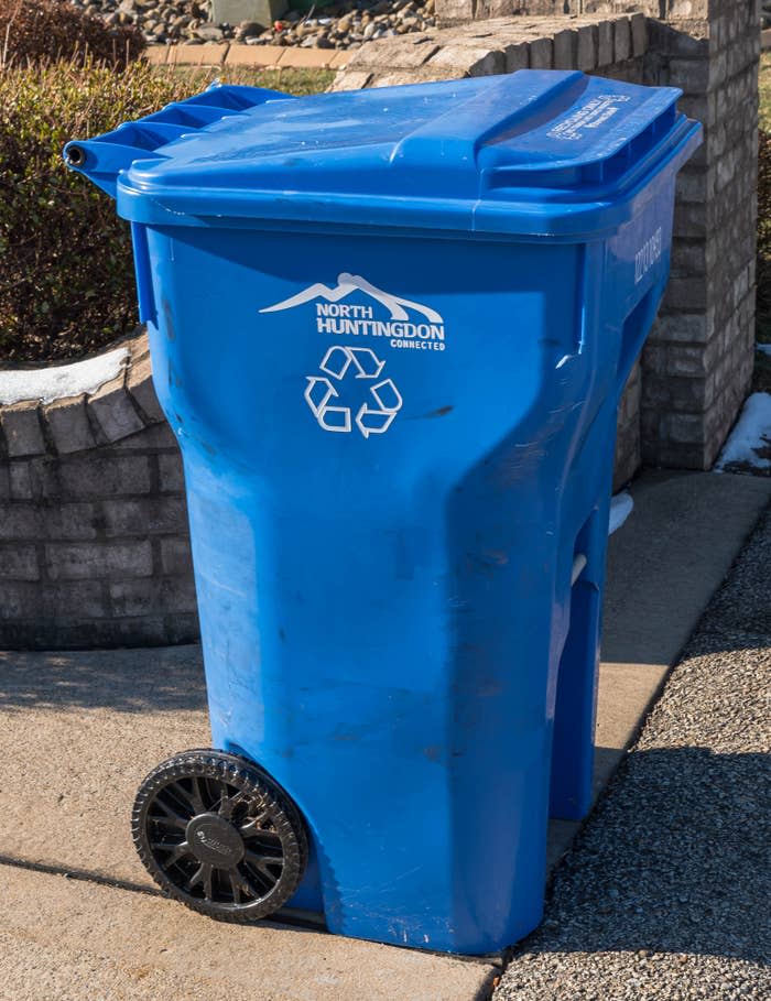 A recycling bin for North Huntingdon Township, placed next to a brick wall and on the pavement