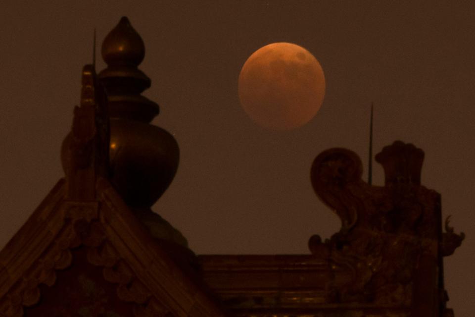 The moon rises behind a corner tower along the outer walls of the Forbidden City during a lunar eclipse in Beijing, Tuesday, Nov. 8, 2022.