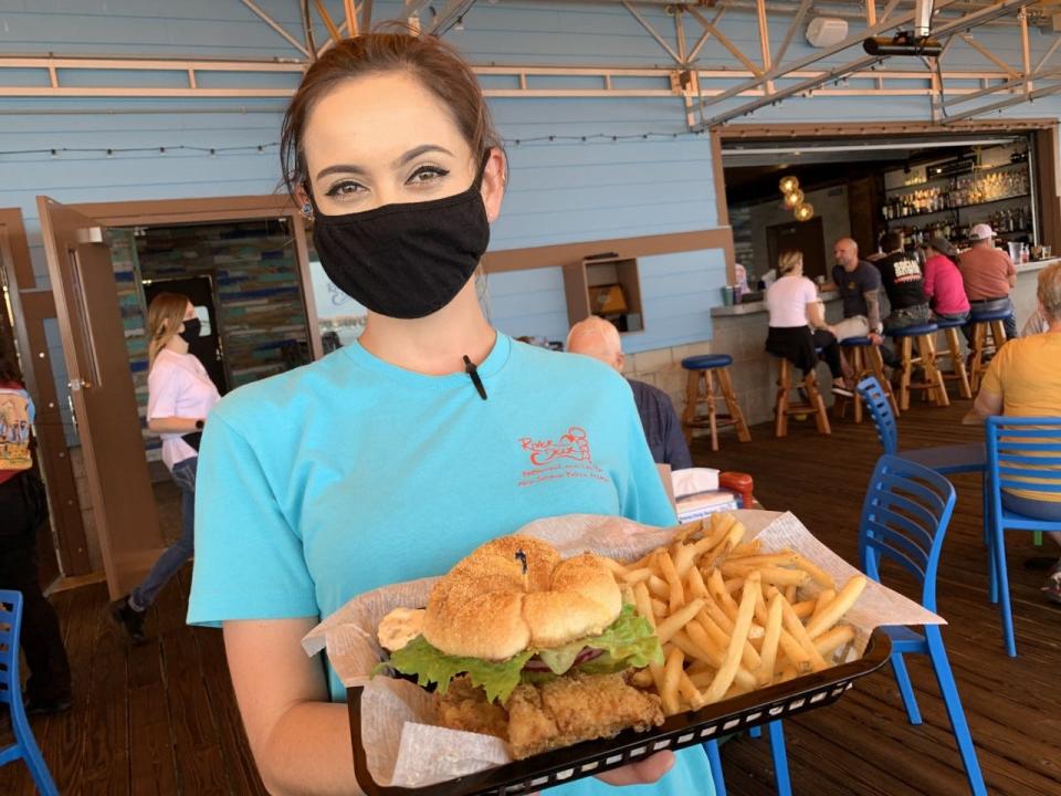 Ashley Rogers, a server at the new River Deck New Smyrna Beach restaurant at 107 N. Riverside Drive in downtown New Smyrna Beach, holds an order of a Sea Harvest Fish Sandwich and fries ready to be served to customers on Tuesday, Jan. 26, 2021.