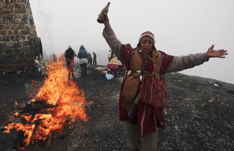 In this Aug. 26, 2012 photo, an Aymara priest holding alcohol for the fire attends a ceremony in honor of the "Pachamama," or Mother Earth, on El Cumbre mountain, considered sacred, on the outskirts of La Paz, Bolivia.  During the month of August, people gather on mountains considered sacred to make offerings and ask for wealth to Mother Earth.  According to local agrarian tradition, Mother Earth awakes hungry and thirsty in August and needs offerings of food and drink in order for her to be fertile and yield abundant crops. (AP Photo/Juan Karita)