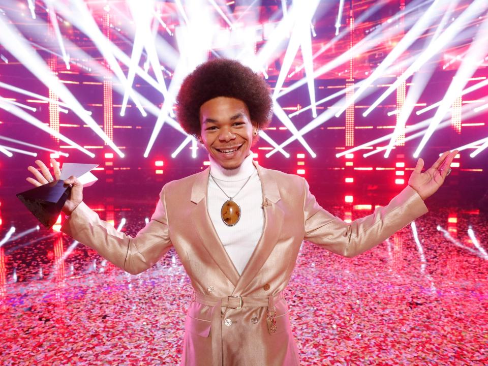 Cam Anthony holding his winning trophy in front of a red, strobe-light background on "The Voice"