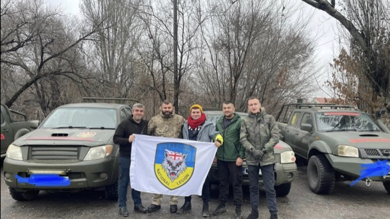 Five men stand in front of vehicles meant for the Ukrainian front. 