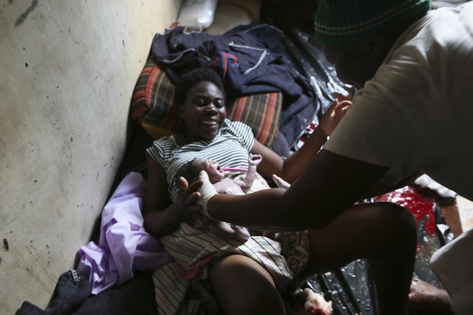 Samantha Nazarere smiles as she is handed her new baby, delivered in a tiny apartment in the poor Mbare suburb in Harare, Zimbabwe, Saturday, Nov. 16, 2019, with the help of 72-year old grandmother Esther Zinyoro Gwena. Grandmother Esther Zinyoro Gwena claims to be guided by the holy spirit and has become a local hero, as the country’s economic crisis forces closure of medical facilities, and mothers-to-be seek out untrained birth attendants.(AP Photo/Tsvangirayi Mukwazhi)