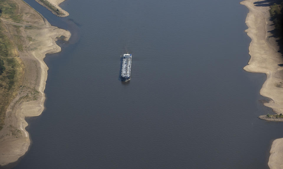 A cargo ship sails on the river Rhine between Cologne and Duesseldorf in Germany, Friday, Aug. 12, 2022. The persistent drought makes the level of the Rhine fall further and further, navigation is only possible to a limited extent. The river levels continue to fall and bring a burden on shipping and nature. (Christoph Reichwein/dpa via AP)