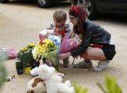 A mother and child place flowers outside a house where the bodies of three children were found, in New Malden, southwest London April 23, 2014. A 43-year-old woman has been arrested on suspicion on murder after the bodies of three children were found at a house in southwest London, police said on Wednesday. Police said a four-year-old girl and two boys, both aged three, were found dead at a residential address in New Malden on Tuesday evening. REUTERS/Olivia Harris (BRITAIN - Tags: CRIME LAW SOCIETY)