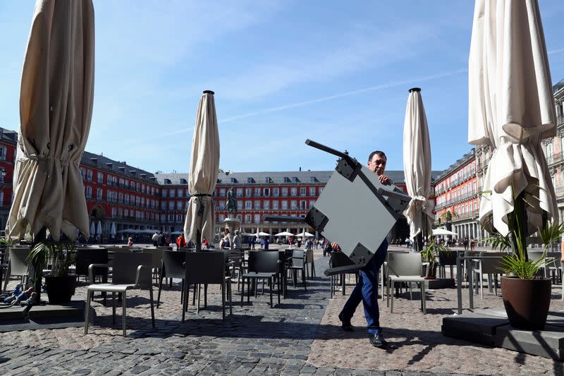 A worker carries a table as he removes the terrace of a restaurant due to the coronavirus outbreak at Plaza Mayor in central Madrid