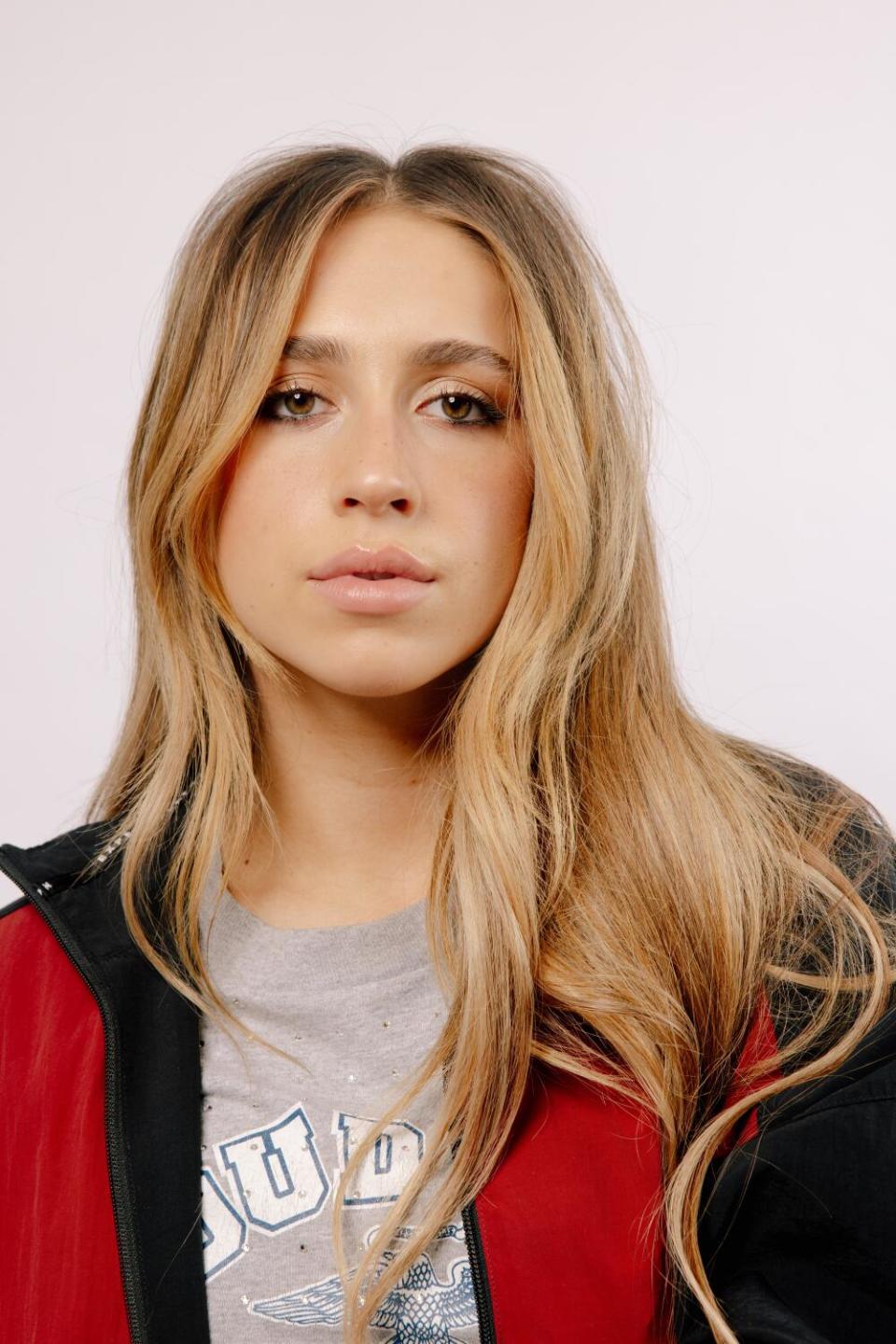 A serious-looking woman with light brown long hair in a T-shirt and jacket.