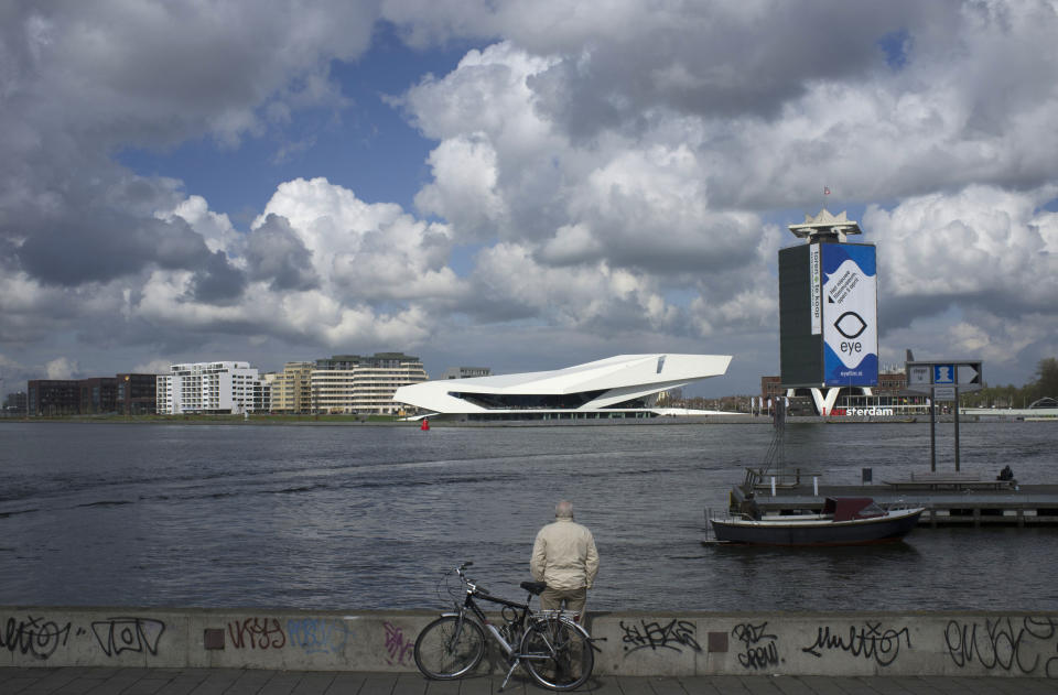 FILE - In this April 21, 2012 file photo, a man admires the new EYE Film Institute, center in white, on the other side of IJ river in Amsterdam, Netherlands. One of Amsterdam's newest landmarks is a stark, white film institute, called the EYE, perched on northern bank of the IJ waterway. While you have to pay to take in a movie, the cafe and its terrace are open to all who are prepared to buy a cup of coffee or light meal and offer a front-row seat to watch barges chug along the IJ against a backdrop of the city skyline. (AP Photo/Peter Dejong)