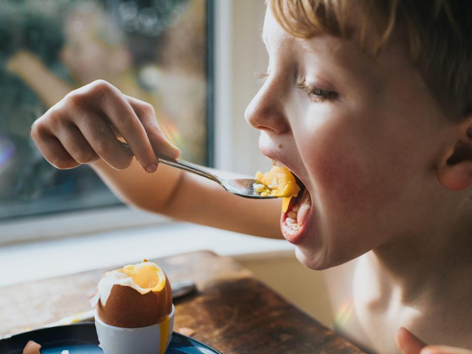 a young boy eating a soft boiled egg with a spoon