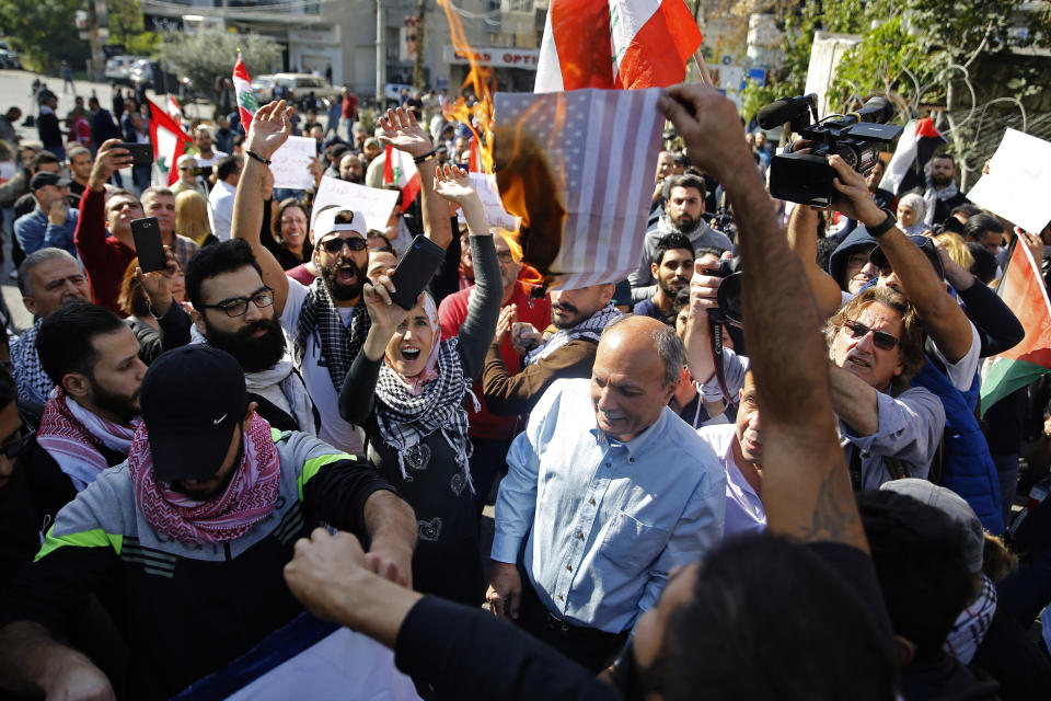 A few dozen people demonstrate and chant slogans as they burn a representation of an American flag during a protest against what they called, "America's intervention in Lebanon's affairs," near the U.S. embassy in Aukar, northeast of Beirut, Lebanon, Sunday, Nov. 24, 2019. Lebanese troops and riot police took tight measures Sunday near the embassy. (AP Photo/Bilal Hussein)