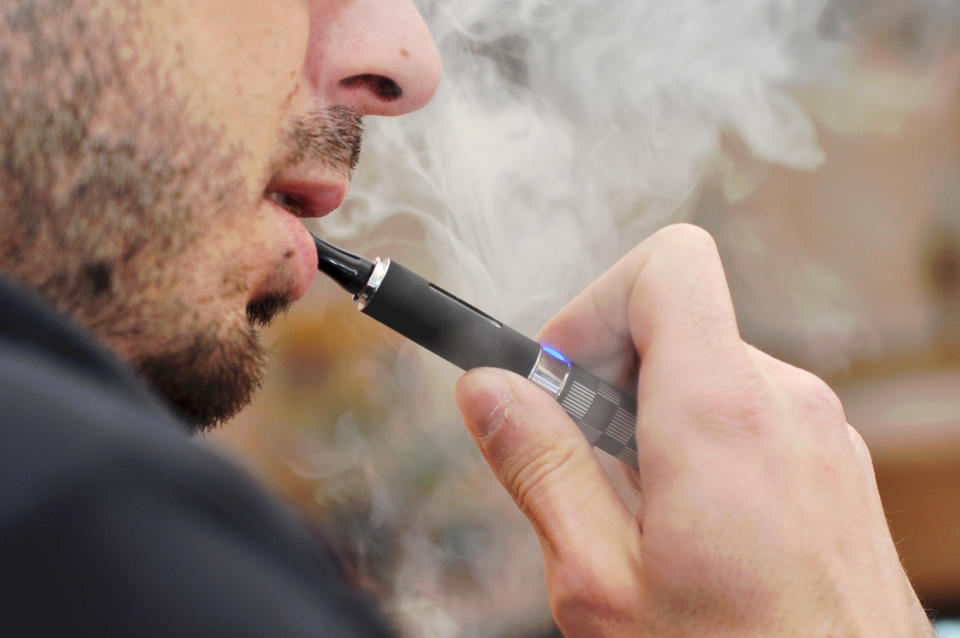 A person vaping, holding an electronic cigarette close to their lips, with vapor visible around their face