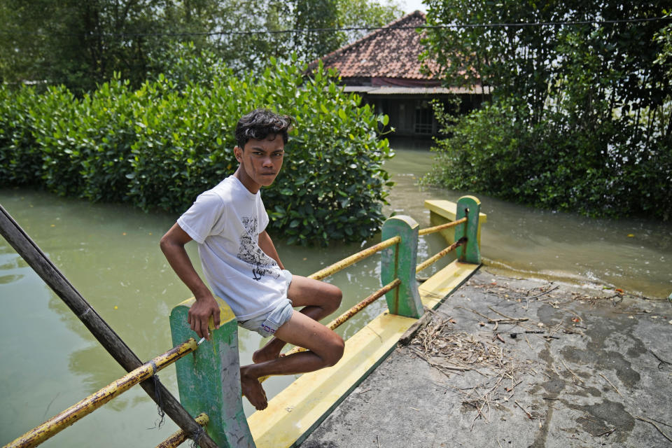 Un niño fotografiado en un puente, frente a una casa abandonada en Mondoliko (Java, Indonesia) el 5 de septiembre del 2022. La vivienda quedó inhabitable por la crecida del mar y sus ocupantes tuvieron que irse de la aldea. (AP Photo/Dita Alangkara)