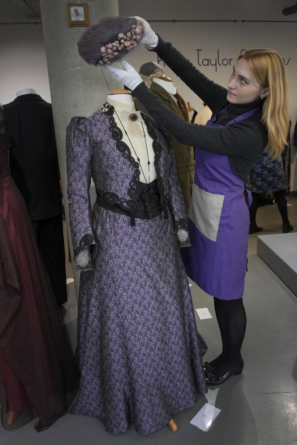 A costume handler arranges Dame Maggie Smith's costume as Violet Dowager, Countess of Grantham in Downton Abbey 2010, at Kerry Taylor Auctions in London, Tuesday, Feb. 27, 2024. The costume estimated at 800-1,200 UK Pounds (1,000-1,500 US Dollars) is one of 69 that will be for auction in the Lights Camera Auction event on March 5. The costumes have been donated by Cosprop in support of The Bright Foundation, an arts education charity, established and funded by John Bright, to provide life-enhancing, creative experiences for children and young people facing disadvantage. (AP Photo/Kirsty Wigglesworth)
