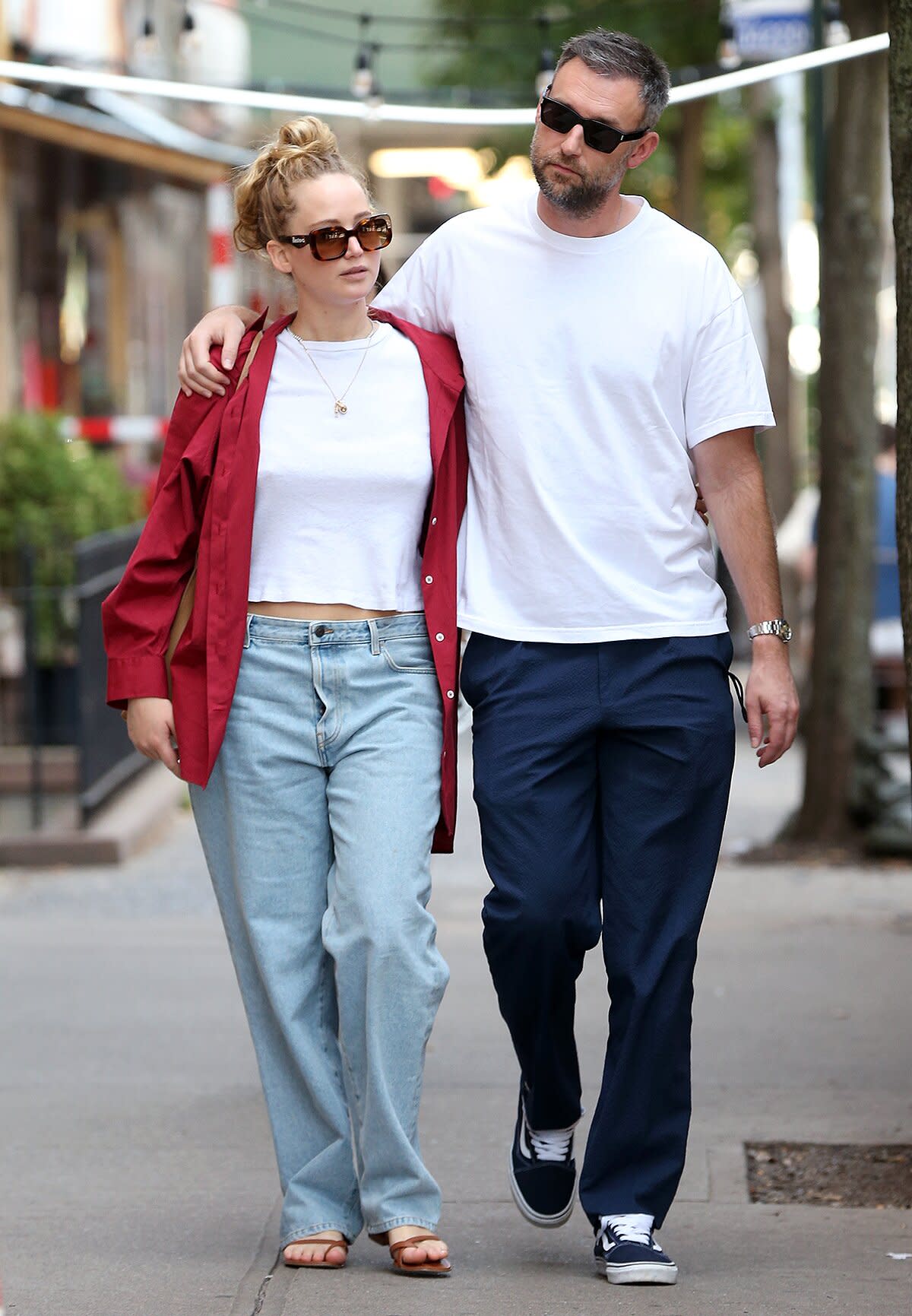 Jennifer Lawrence is seen wearing Illesteva sunglasses, crop top, jeans, red shirt and sandals with Cooke Maroney in New York City