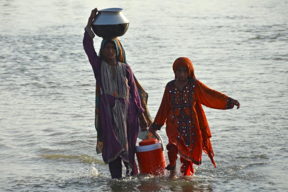 Flood-affected women carry drinking water in containers after fleeing from their homes following heavy monsoon rains in the Sohbatpur area in Jafarabad district of Balochistan province (AFP via Getty Images)