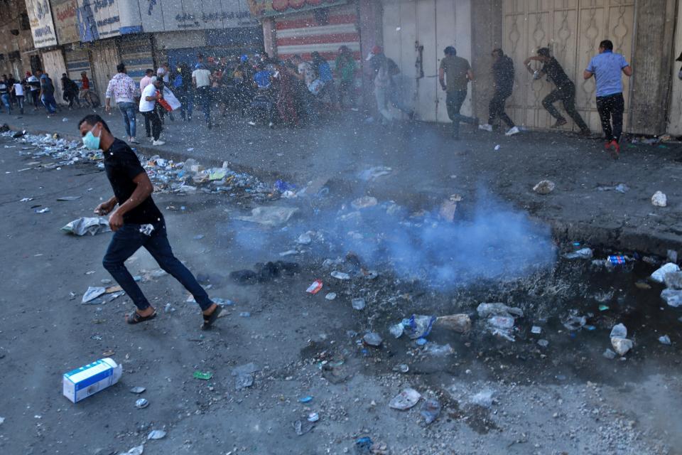 Protesters run for cover while riot police fire tear gas during clashes between Iraqi security forces and anti-government protesters in Baghdad, Iraq, Monday, Nov. 11, 2019. (AP Photo/Khalid Mohammed)