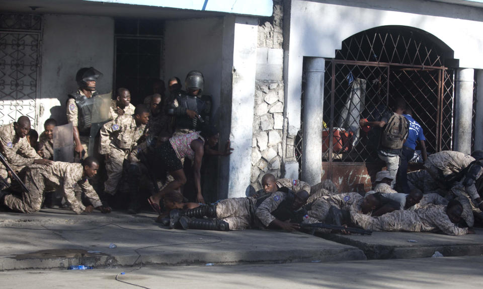 Agentes de la Policía Nacional se cubren tras un tiroteo al final de una ceremonia que conmemora el aniversario del asesinato del héroe de la independencia en Puerto Príncipe, Haití, el miércoles 17 de octubre de 2018. (AP Foto / Dieu Nalio Chery)