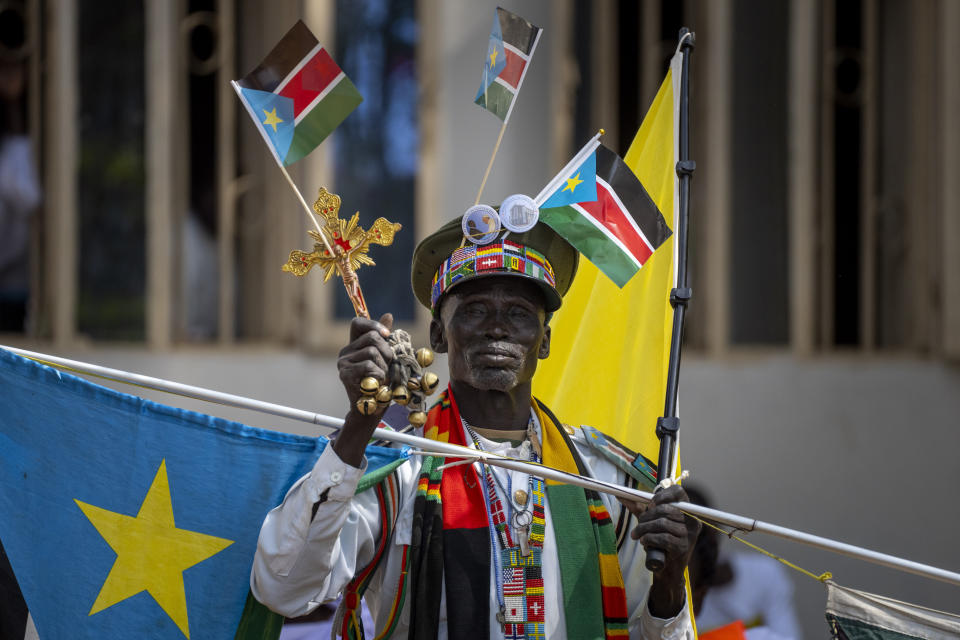 A man holds national flags and other items as he waits for Pope Francis to leave after addressing clergy at the St. Theresa Cathedral in Juba, South Sudan, Saturday, Feb. 4, 2023. Pope Francis is in South Sudan on the second leg of a six-day trip that started in Congo, hoping to bring comfort and encouragement to two countries that have been riven by poverty, conflicts and what he calls a "colonialist mentality" that has exploited Africa for centuries. (AP Photo/Ben Curtis)