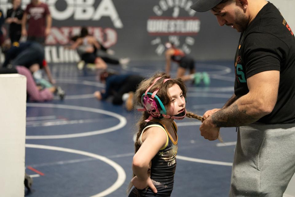 Feb 14, 2024; Fairfield, NJ, United States; (Center) Quinn Cannici, a 7-year-old wrestler from Oakland, is on track to win a coveted Trinity Award if she finishes first at the Reno Worlds in April. Cannici’s father Glen Cannici secures the end of a braid with a hair tie during practice at Cordoba Trained Wrestling Club.