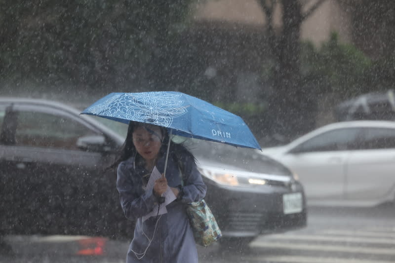 氣象署18日表示，19日台灣北部海面鋒面逐漸遠離，但大台北仍有局部大雨發生的機會。圖為台北市中正區大雨，民眾撐傘過馬路。（中央社）