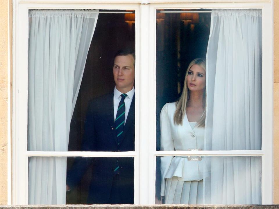 Jared Kushner and Ivanka Trump look outside of a window with white curtains pulled aside.