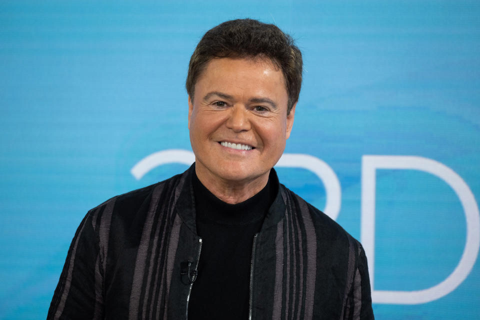 Donny smiling, wearing a black pinstripe zip up blazer over a black turtleneck