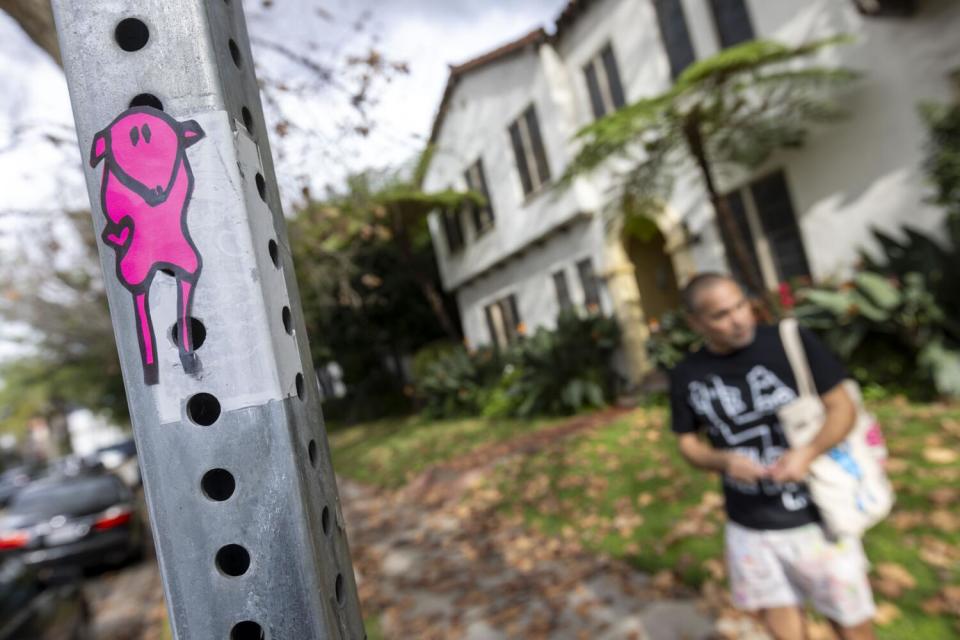 A man stands behind a post that has a pink cartoon sheep pasted on it.