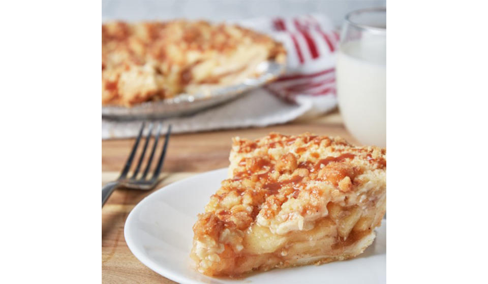 Slice of fresh apple pie with crumble and caramel topping on a white plate. 