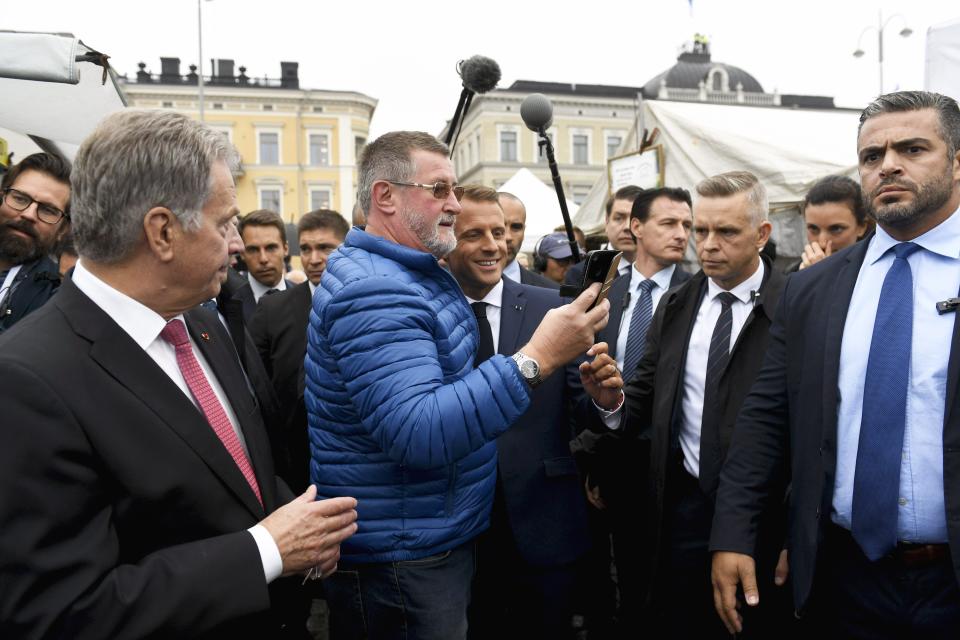 France's President Emmanuel Macron, centre right, take a selfie with a member of the public as Finland's President Sauli Niinisto, left, looks on, at a local market, outside the Presidential Palace after their joint press conference in Helsinki, Finland, Thursday Aug. 30, 2018. Macron is in Finland on a two-day official visit. (Antti Aimo-Koivisto/Lehtikuva via AP)